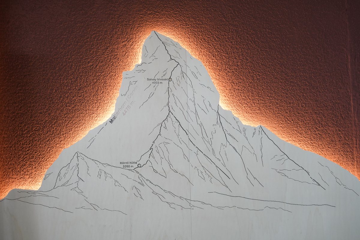 Silhouette de montagne rétroéclairée sur le mur rouge du CUBE Store Valbirse